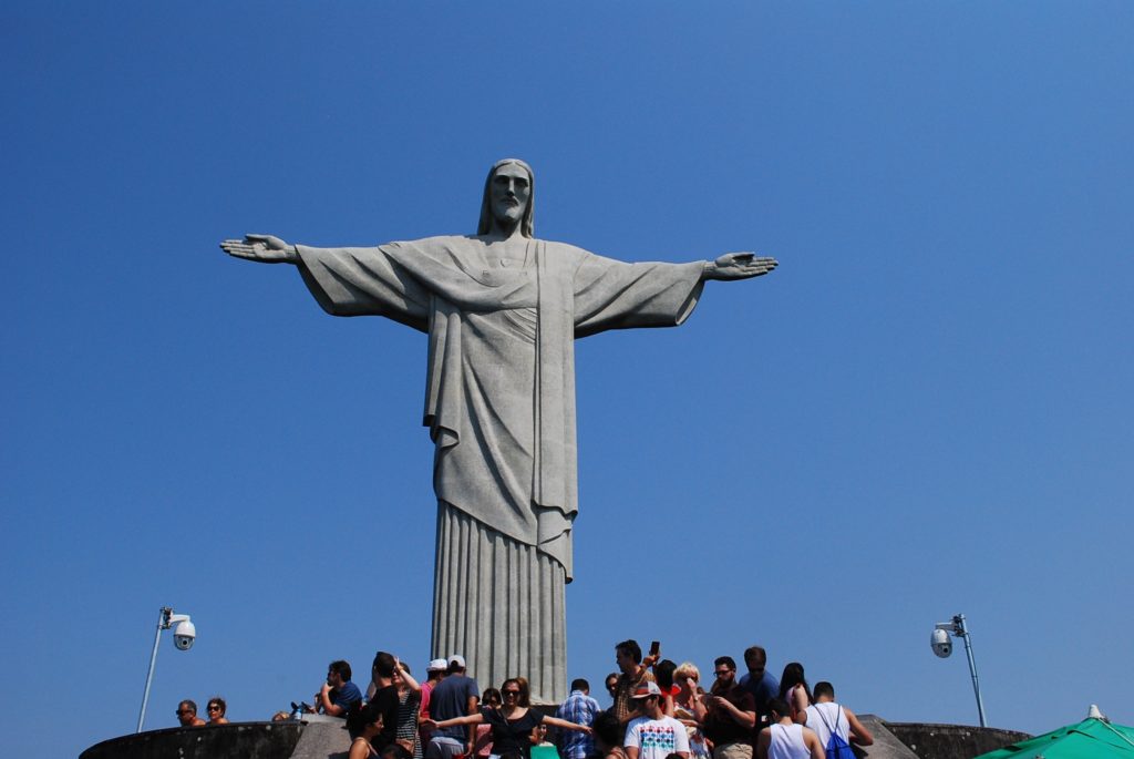 Christ the Redeemer statue overlooking Rio de Janeiro, with visitors gathered at its base beneath a clear blue sky.