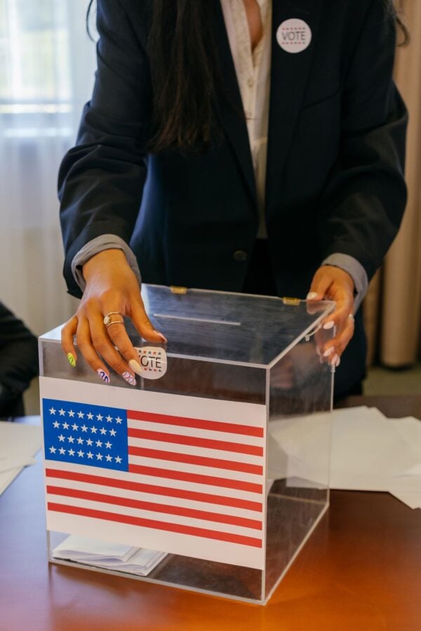 Voting Rights and Democratic Participation Person placing a paper ballot into a transparent ballot box displaying an American flag