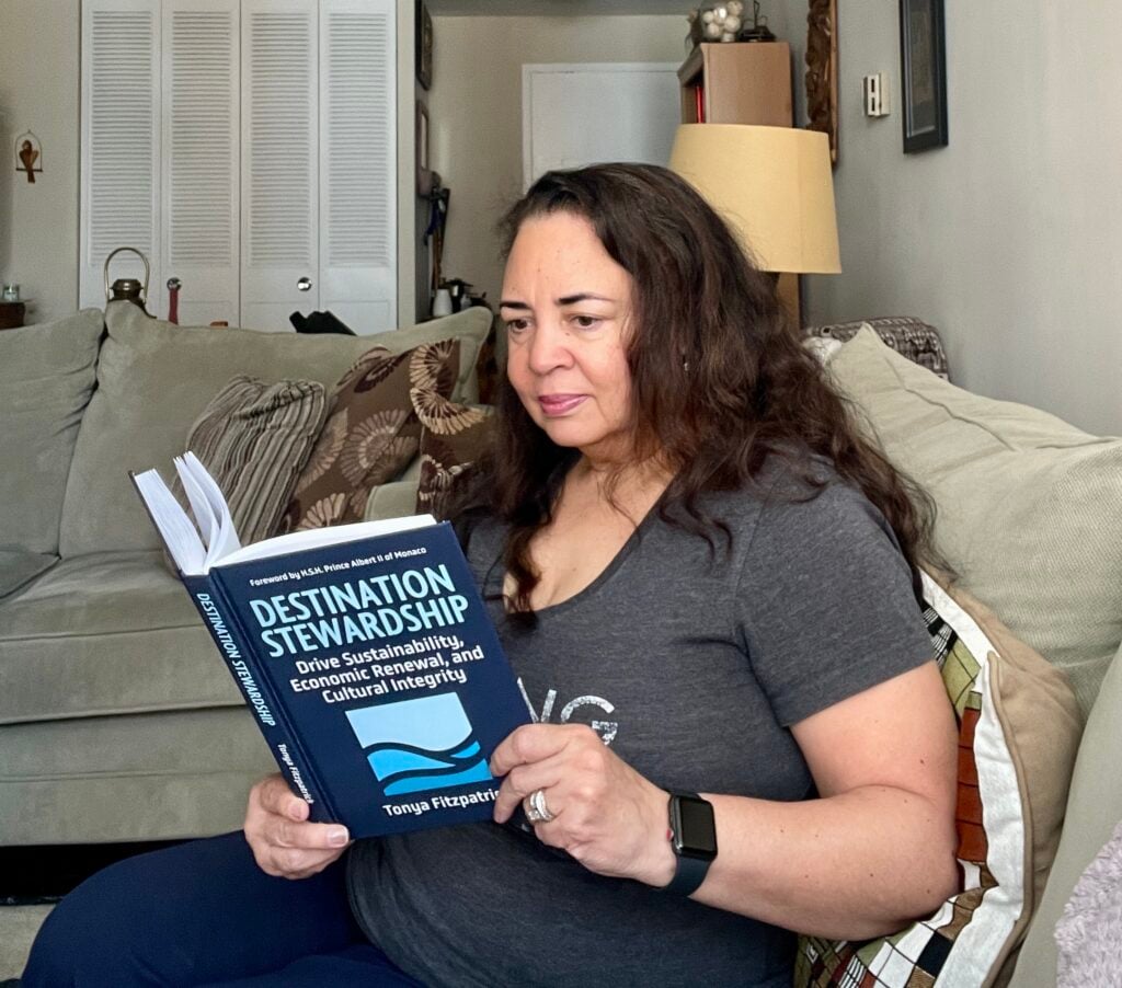 Tonya reading her copy of Destination Stewardship sitting on the couch in a living room.