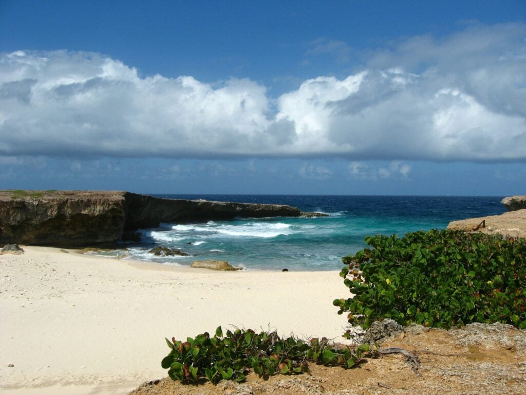 a sandy beach with blue water and white clouds form the backdrop to the natural pool in Arikok National Park.