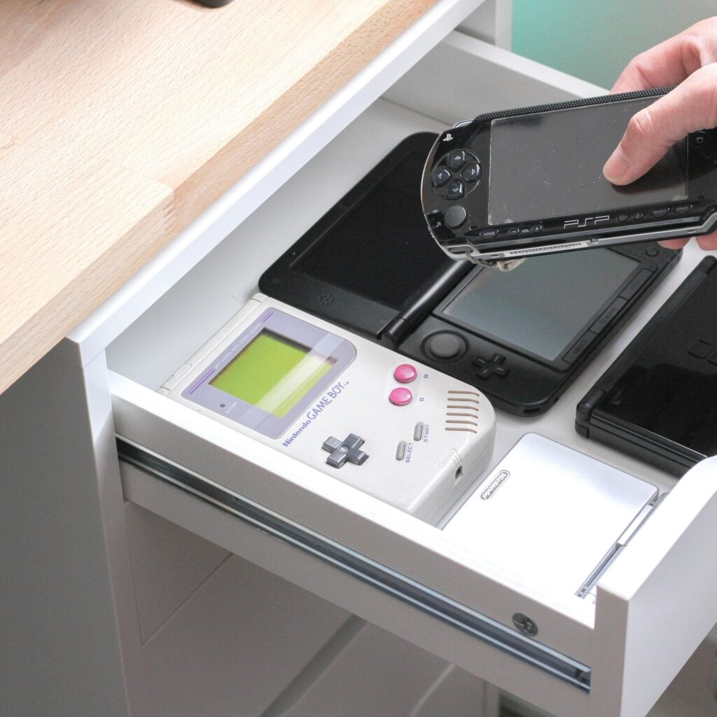 Photo by Andrew M six handheld game consoles and phone being tucked into a drawer.