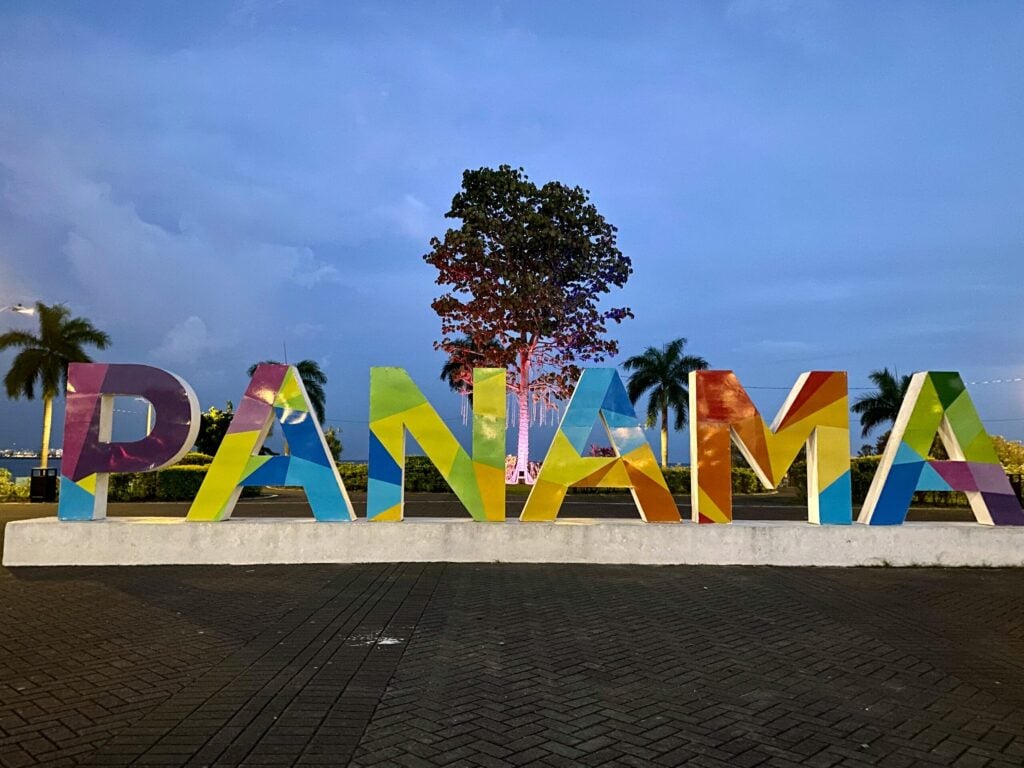 Colorful PANAMA sign along a waterfront promenade at dusk with a tree in the background