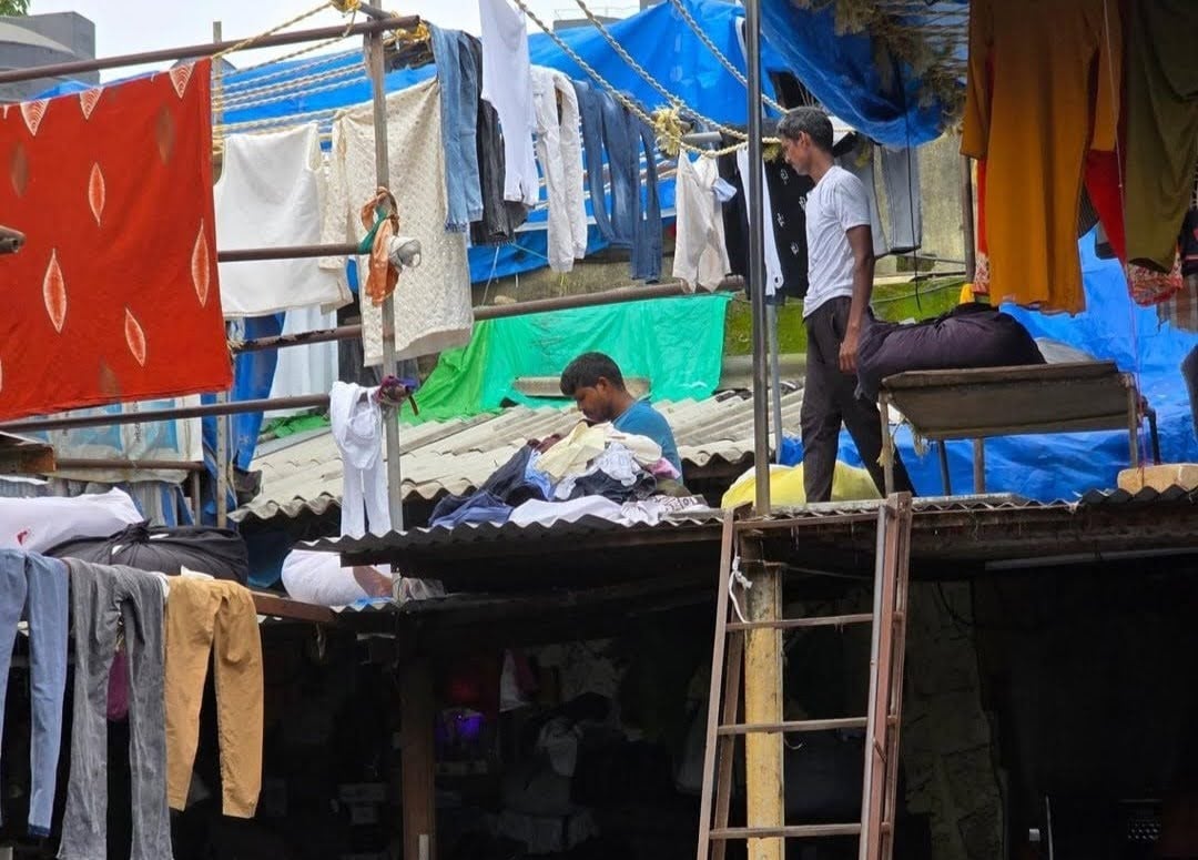 Two workers pull laundry off the clotheslines on a rooftop