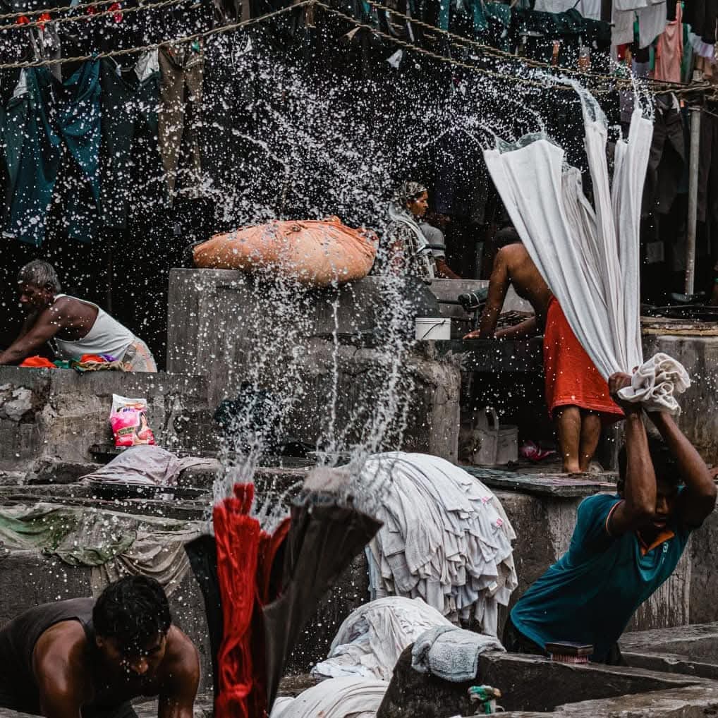 Water flies in all directions as workers beat wet laundry against the stone 